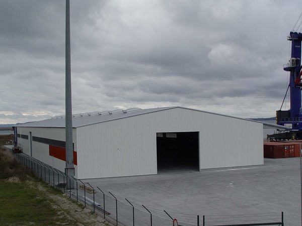 Außenansicht der neu gebauten Lagerhalle mit weißer Fassade und geöffnetem Sektionaltor